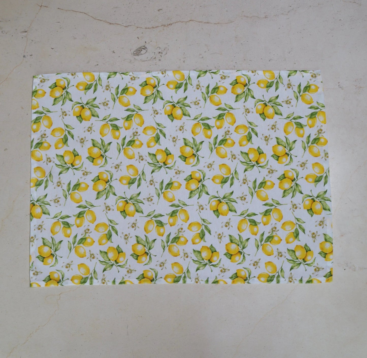 Mantel individual con estampado de limones amarillos sobre fondo blanco sobre mesa de mármol