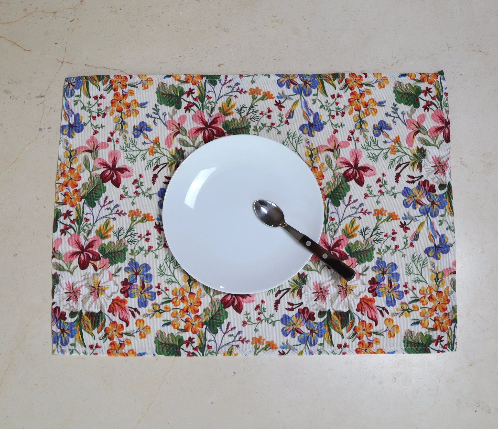 Mantel individual con flores multicolor con vajilla blanca sobre mesa

