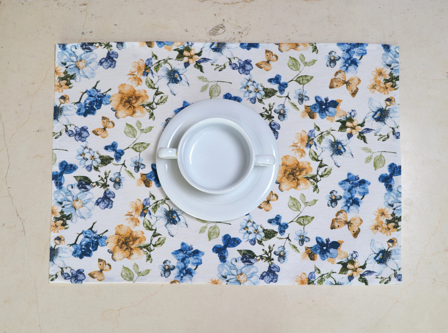 Mantel individual con flores azules y blancas con vajilla blanca sobre mesa
