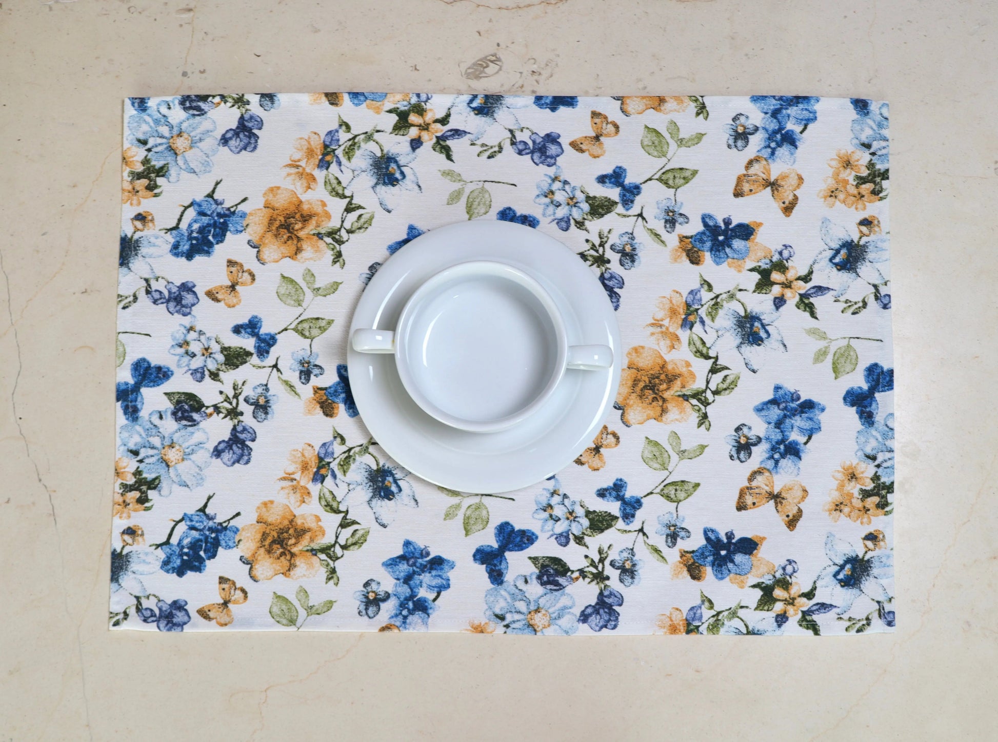 Mantel individual con flores azules y blancas con vajilla blanca sobre mesa
