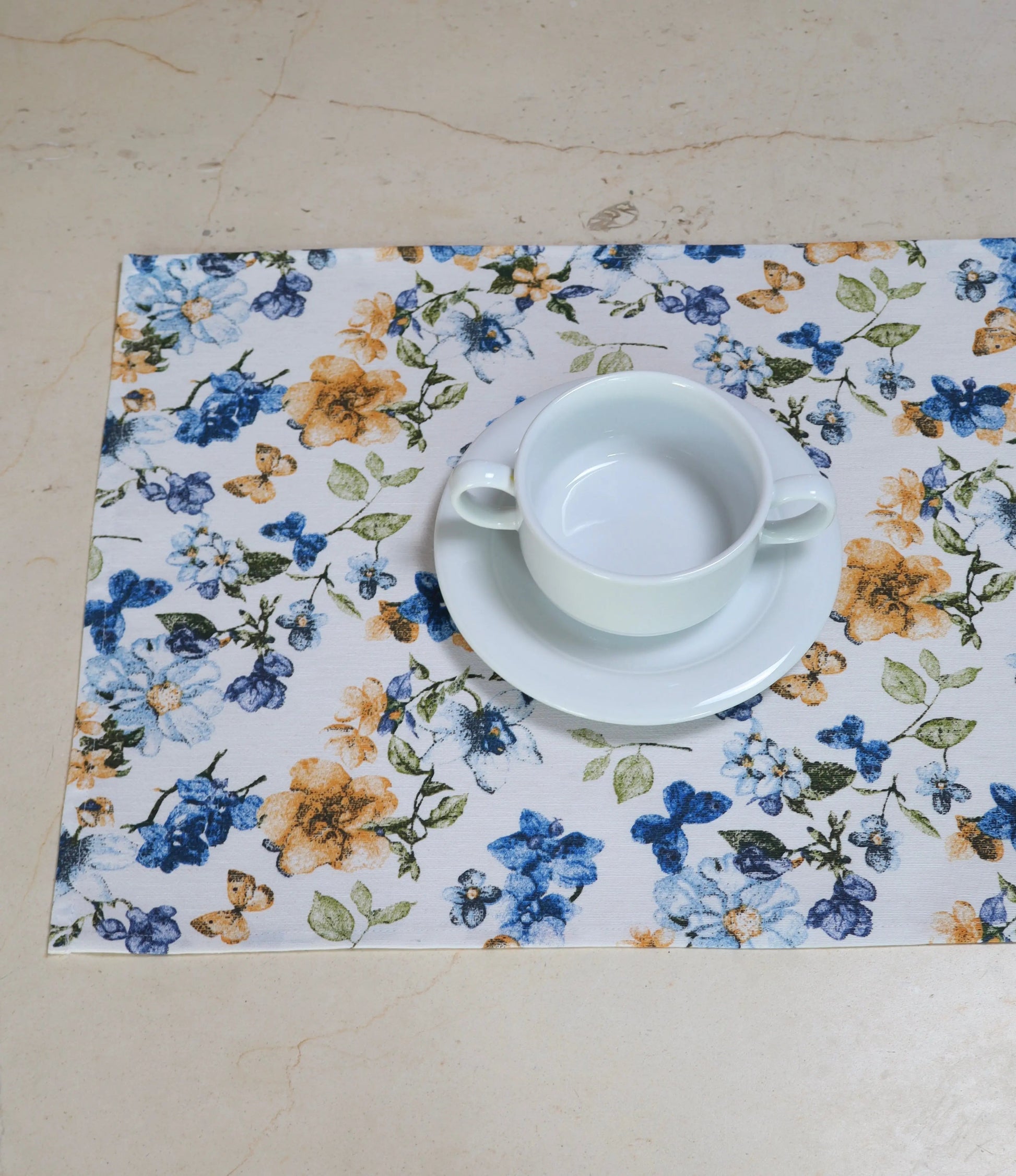Mantel individual flores azules como parte de mesa decorada con vajilla blanca 
