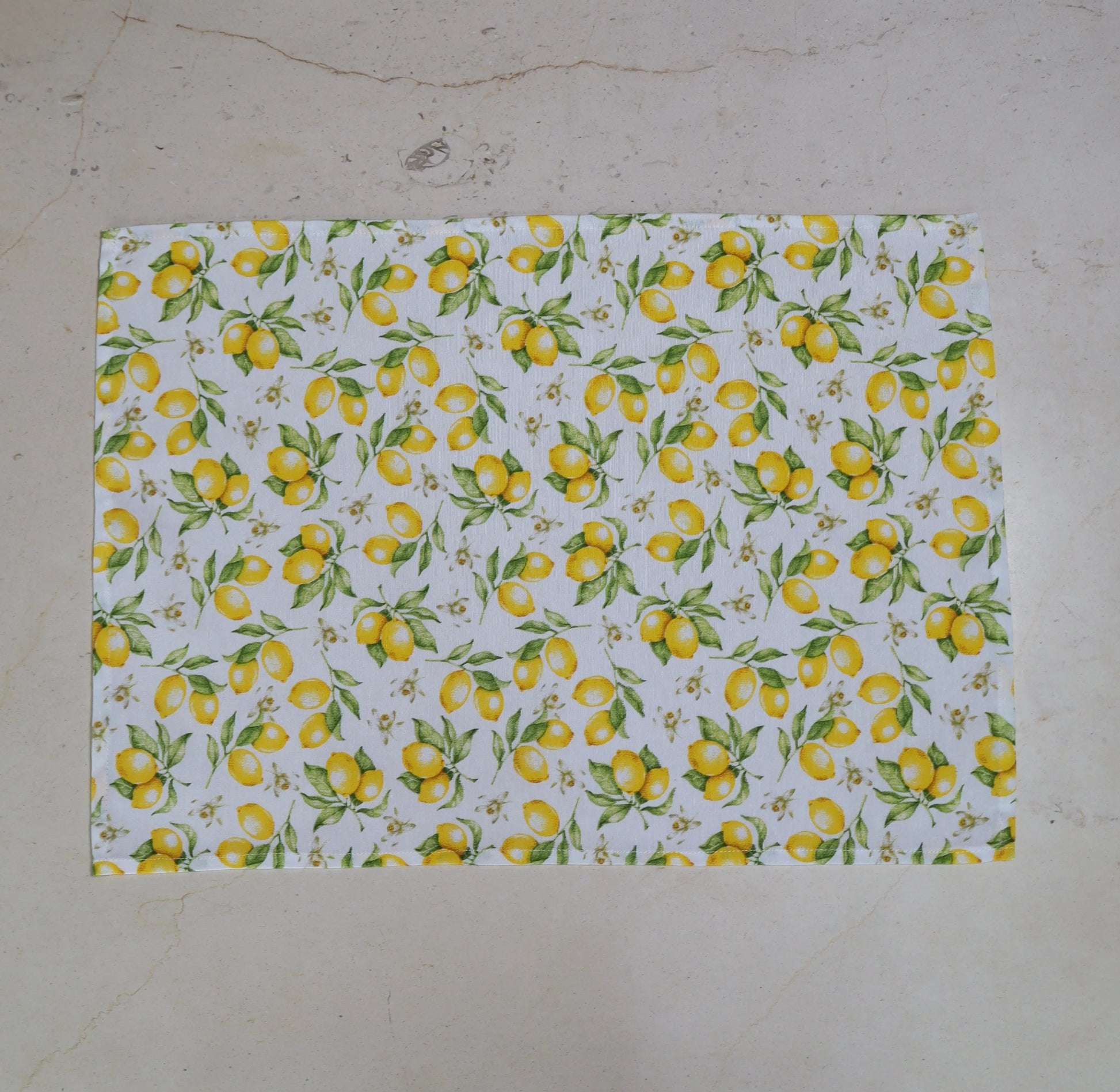  Mantel individual con estampado de limones amarillos sobre fondo blanco sobre mesa de mármol
